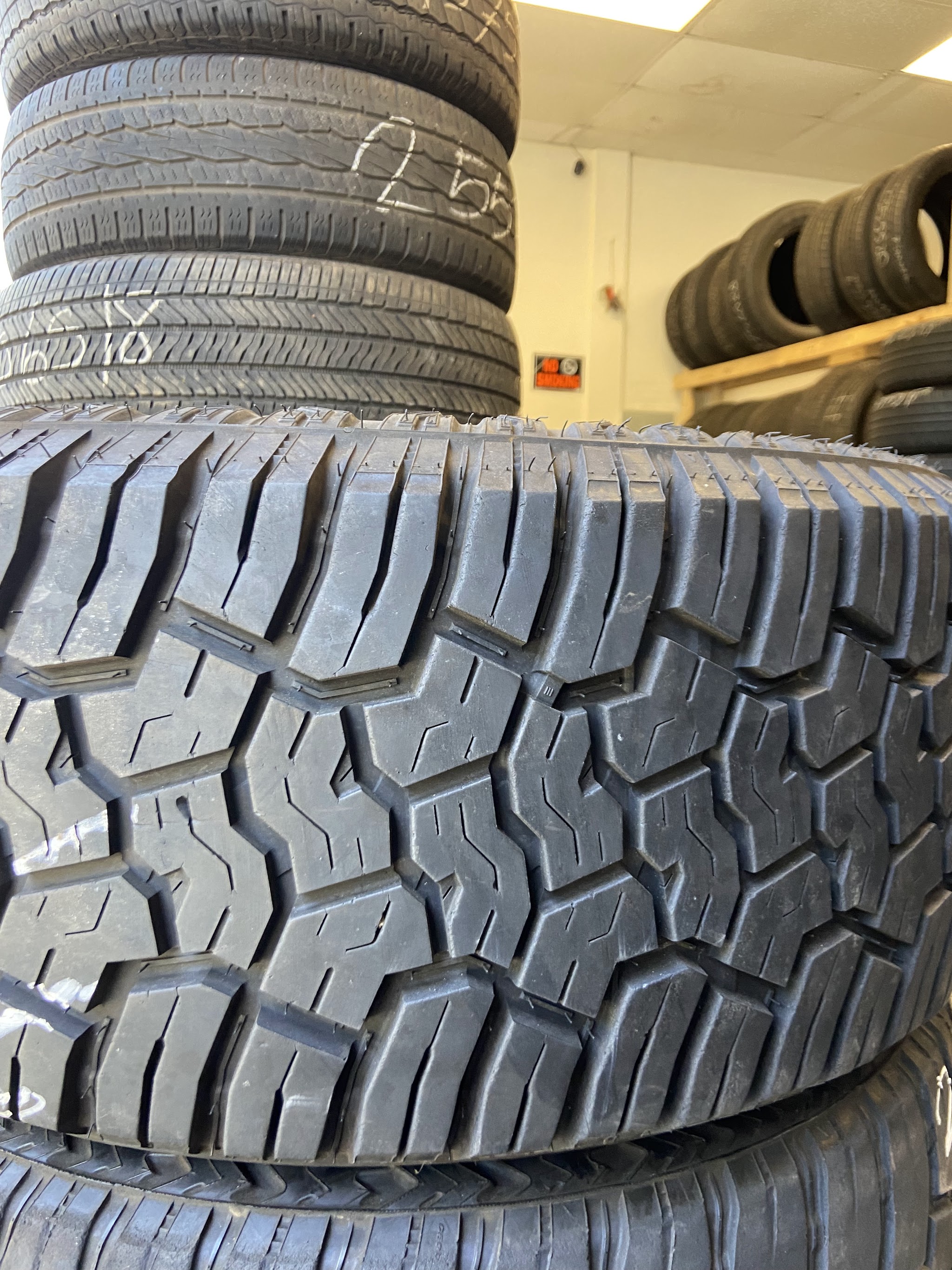 Close-up of an all-terrain tire with used tires stacked behind it